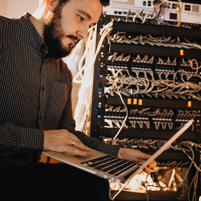 An image of a man working on a laptop in a server room | Network Support in Falkirk