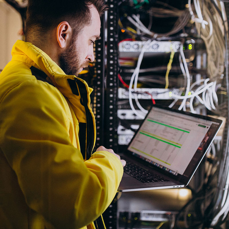 An image of a man working on a laptop in a server room | Remote IT Support in Falkirk