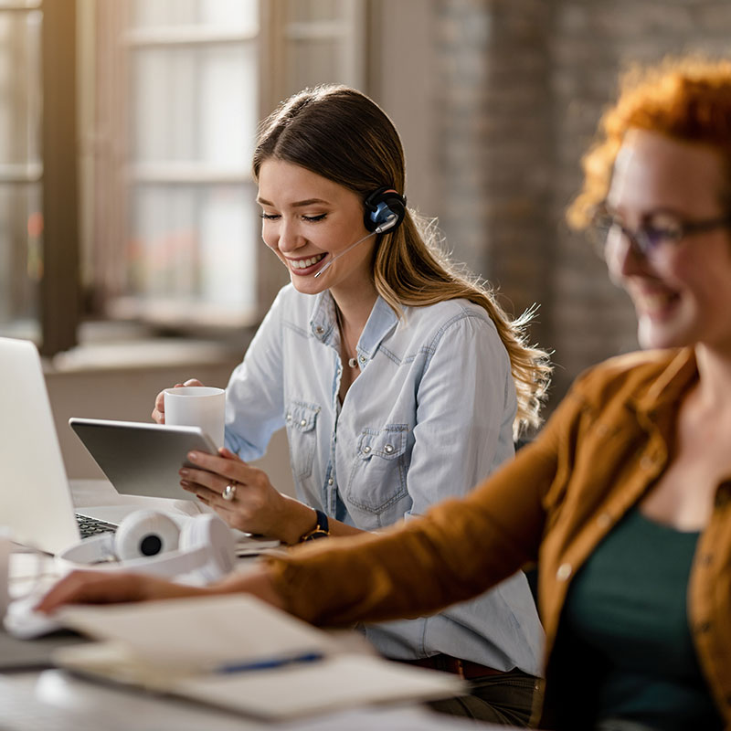 Am image of two women in an office, one holding a laptop and wearing a headset | Remote IT Support in Falkirk